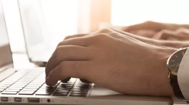Image shows a close up of a person typing on their laptop