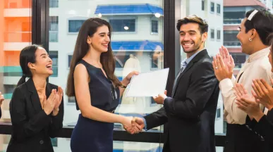 Image shows a coworker presenting an award to another coworker in front of a group of teammates.