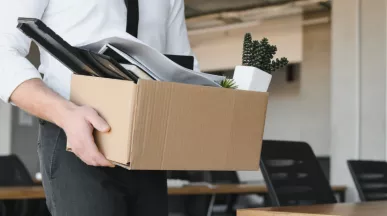 Image shows a person leaving an office with a box of items.