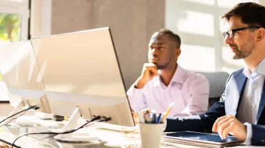 Two employees happily looking at a computer screen at their desk