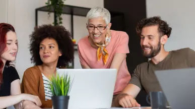 Four employees in varying generations working together at a computer at work.